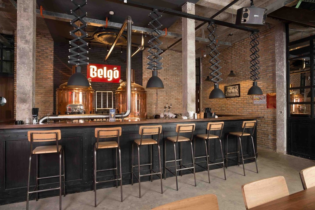 Balcão de bar industrial, seis banquetas de madeira, luminárias pendentes, parede de tijolos