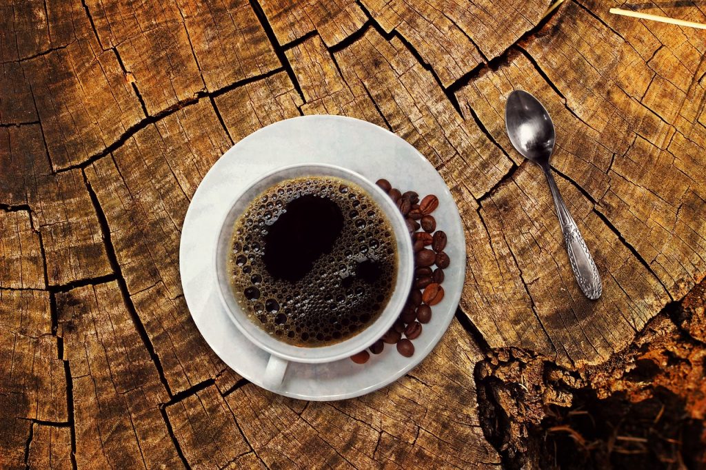 Xícara de café com grãos de café no pires, colher de café, tronco de árvore