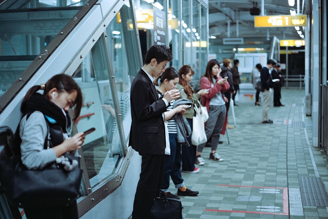 Pessoas paradas na plataforma de trem olhando seus smartphones