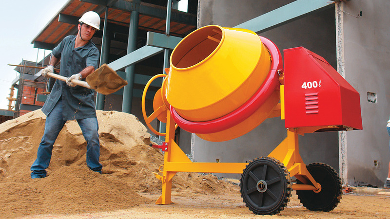 Trabalhador em obra colocando areia em betoneira