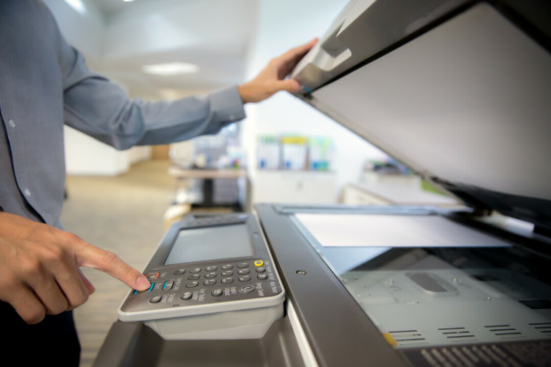 Homem com camisa social em uma empresa. Ele está teclando os botões de uma impressora.