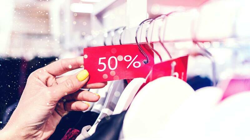 Uma mão segurando cupom vermelho de 50% afixado em cabide de roupas