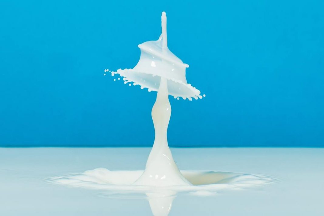 Gota de leite caindo em superfície com mais leite à frente de um fundo azul