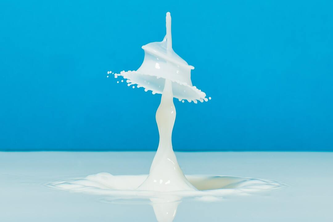 Gota de leite caindo em superfície com mais leite à frente de um fundo azul