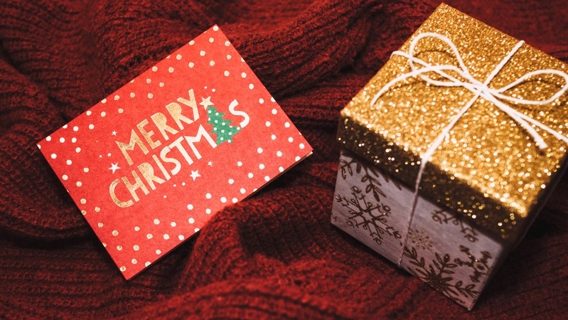 Cartão de natal ao lado de caixa dourada com laço.
