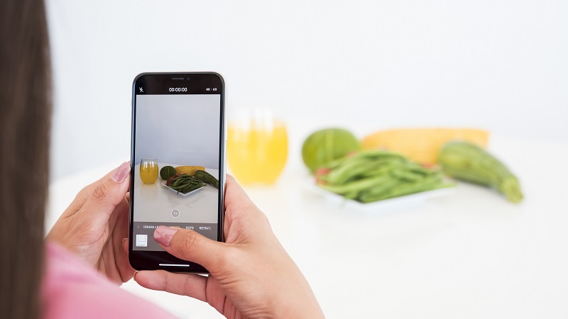 Mulher tirando foto de vegetais usando celular fundo branco