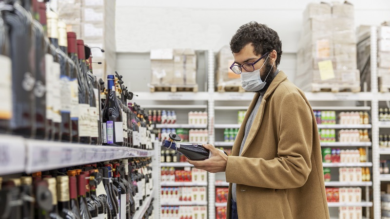homem de máscara em supermercado escolhendo bebida